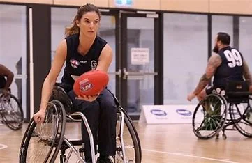 Yasmina holding an AFL football while playing wheelchair football on an indoor court.